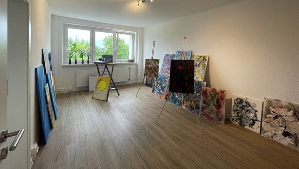 Uno studio d'arte con cavalletti, dipinti, una finestra vista e un termosifone.