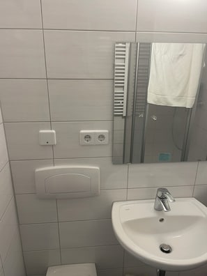 Une salle de bain avec un lavabo blanc, un miroir, un porte-serviettes et des toilettes.
