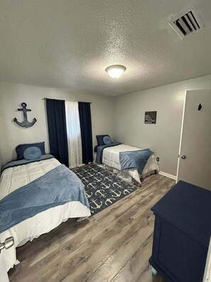Ein Schlafzimmer mit zwei Betten, einem kleinen Schreibtisch, einer Tür und einer Wandleuchte.