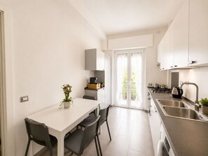 Una cocina moderna con comedor, muebles blancos, una cafetera y vistas a través de un ventanal.