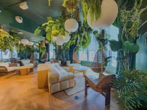 Ein moderner Lounge-Bereich mit einer Couch, Sesseln, hängenden Pflanzgefäßen und Blick auf die Stadt.