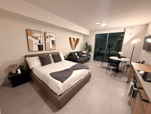 Ein modernes Hotelzimmer mit einem großen Bett, einer Sitzecke, einem Essbereich und einer Glastür zum Balkon.