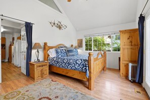 Ein Schlafzimmer mit einem hölzernen Bett, einem Nachttisch, einem Fenster mit Ausblick und einer Heizung.