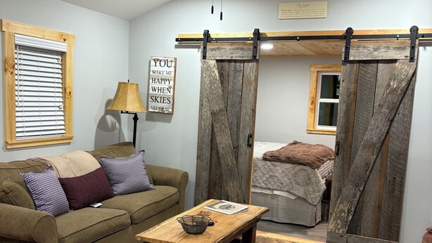 Een gezellige woonkamer met een bank, een bijzettafeltje, een plafondventilator en een schuifdeur in boerderijstijl.
