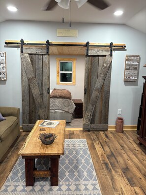 A room with a bed, a wooden table, a small rug, and a window.
