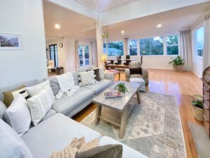A modern living room with a sofa, coffee table, and a view of the outdoors through large windows.