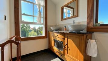 A bathroom with a wooden vanity, two sinks, a mirror, and a window with curtains.
