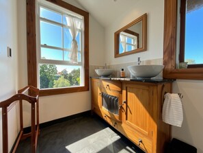 Un baño con tocador de madera, dos lavamanos, un espejo y una ventana con cortinas.