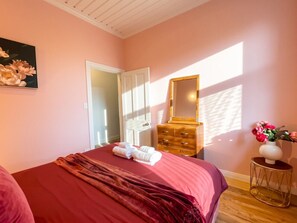 Un dormitorio con cama, cómoda, espejo y un florero con flores.