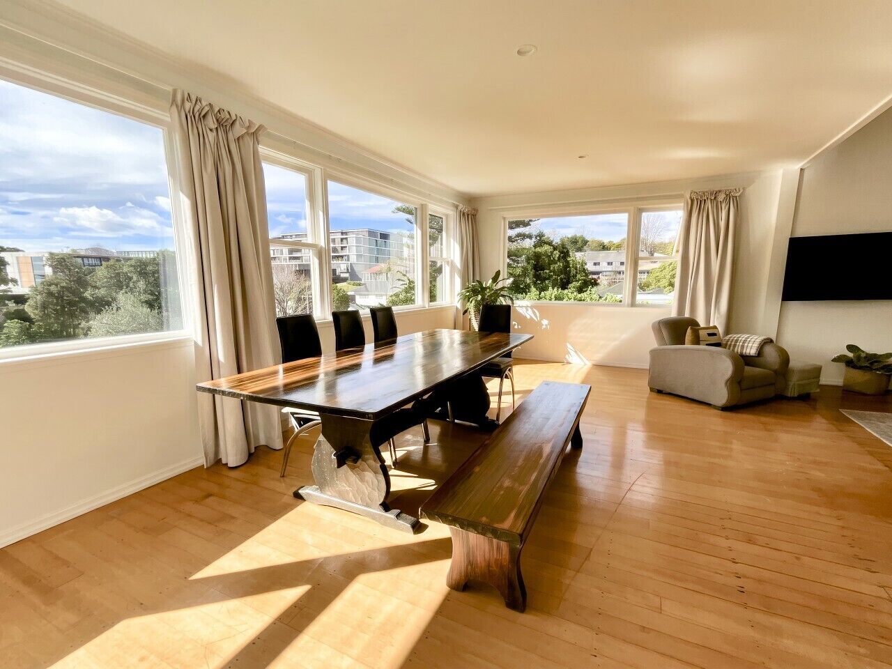 A spacious room with a large dining table, multiple chairs, a bench, a sofa, and a TV.