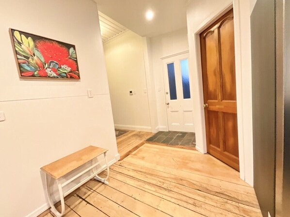 A hallway with wooden flooring, a bench, a door with a blue tint, and a wall-mounted painting.