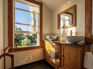 A bathroom with a large window, wooden cabinetry, a sink, and a mirror.