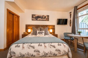 Ein Schlafzimmer mit Bett, Stuhl, Tisch, Fernseher und einem Bild an der Wand.
