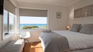 A bedroom with a large window, a bed, a chair, and a bedside table.
