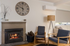 En stue med pejs, et stort vægur, en lampe og en sofa.
