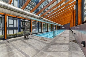 Ein mit modernem Design gestalteter Innenpool, großflächige Fenster und eine Holzbalkendecke.
