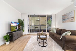 A living room with a TV, sofa, coffee table, and a sliding glass door leading to a balcony. - Evi-3B2B Free Parking! Walk to Casino! Sleeps 8! (Southbank)
