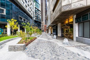 Ein moderner Hotelkorridor in der Stadt mit Glasfassaden, einem zentralen Gehweg und begrünten Bereichen.