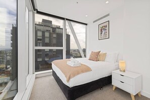 Ein modernes Hotelzimmer mit großem Fenster, einem Bett, einem Nachttisch und einem gerahmten Bild an der Wand.