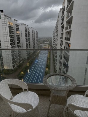 Ein Balkon mit zwei Korbstühlen und einem Glastisch, der auf eine Stadtansicht mit hohen Gebäuden und einer beleuchteten Straße blickt.