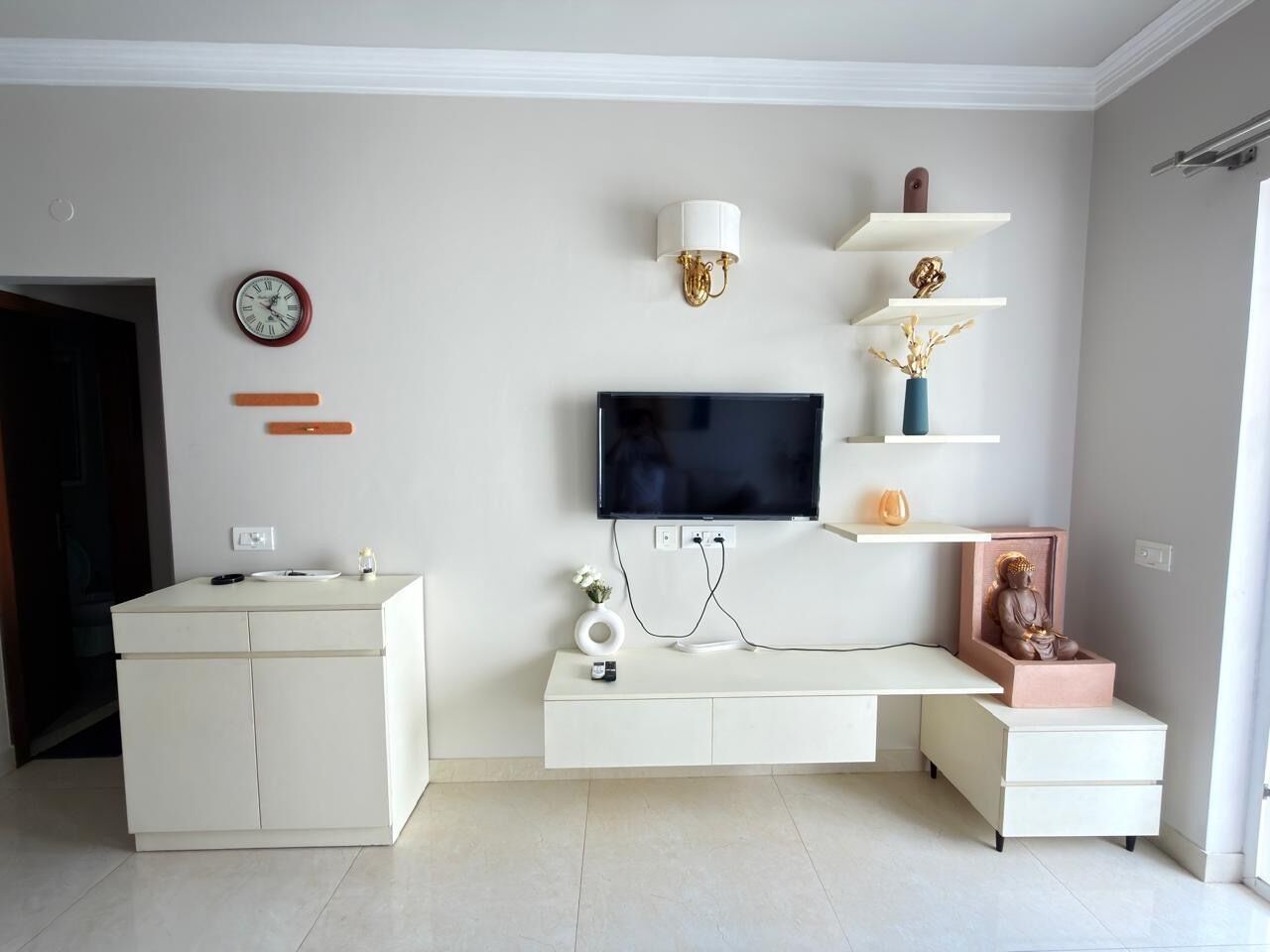 Ein modernes Wohnzimmer mit Flachbildfernseher, weißen Schränken, einer Uhr und Dekoration auf Regalen.