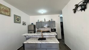 Eine kompakte Küche mit grauen Schränken, einer Marmorarbeitsplatte und einem Edelstahl-Kühlschrank.