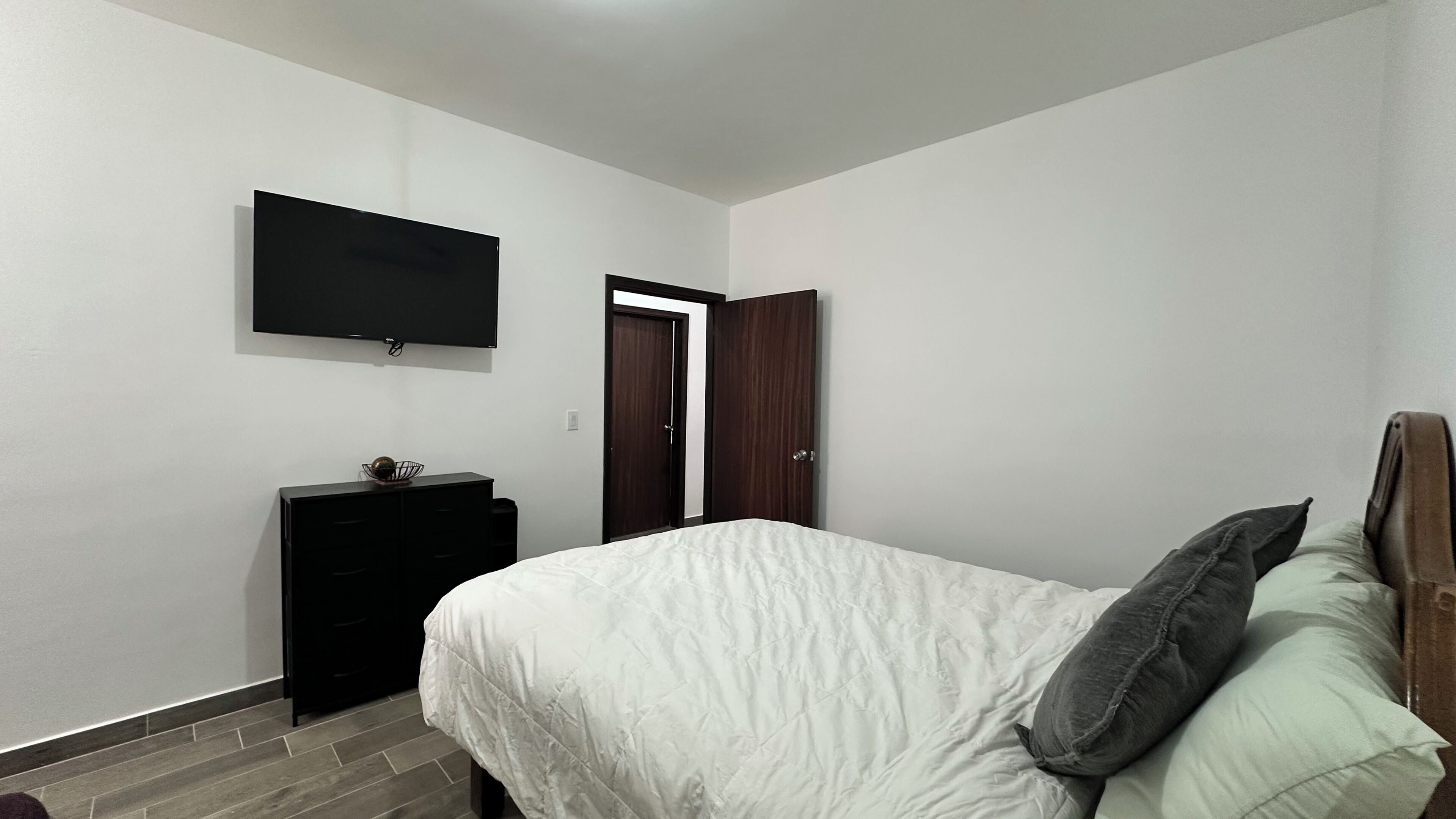 Une chambre à coucher avec un lit, une commode, un téléviseur et une porte.