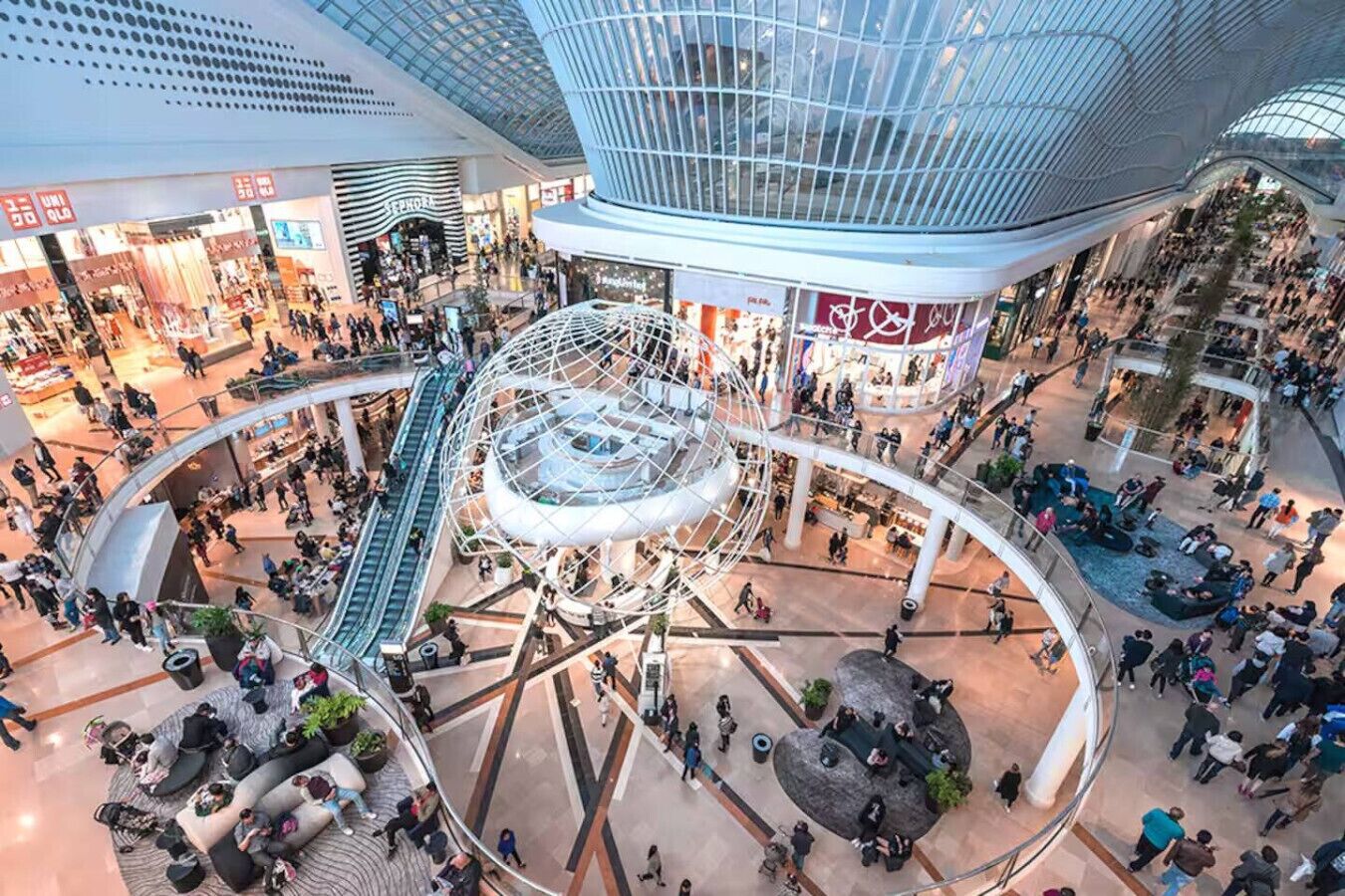 A multi-level shopping mall with a central atrium, escalators, and various retail stores.