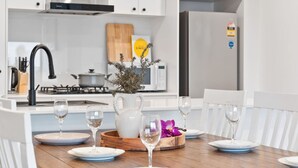 Eine moderne Küche mit weißen Schränken, Edelstahlgeräten und einem Essbereich mit weißen Stühlen und einem Holztisch, gedeckt für eine Mahlzeit.