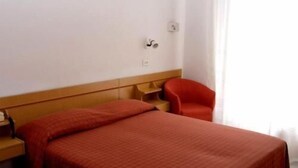A hotel room with a bed, a chair, a nightstand, and a window with curtains. - Hotel San Remo (Riccione)