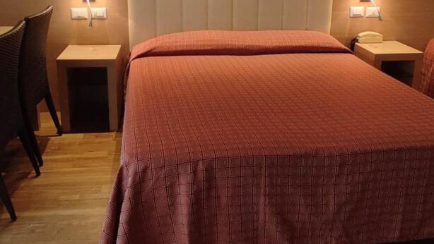 A hotel room with a bed, two bedside tables, a chair, and a wall-mounted lamp. - Hotel San Remo (Riccione)