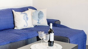 Un letto con lenzuola blu, due cuscini con disegni di cavalluccio marino, una bottiglia di vino e due bicchieri su un tavolo.