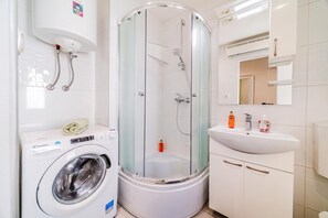 A compact bathroom with a washing machine, a glass-enclosed shower, and a sink. - Zagreb City Center Vibes Near Main Square (Zagreb)
