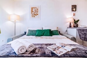 Ein ordentlich bezogenes Bett mit Kissen, einer Lampe, einer Pflanze und einer Zeitschrift auf der Tagesdecke.