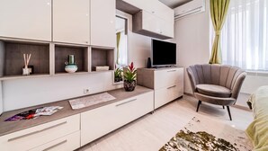 Ett modernt vardagsrum med en platt-TV, en soffa, ett soffbord och en matplats med ett bord och stolar.