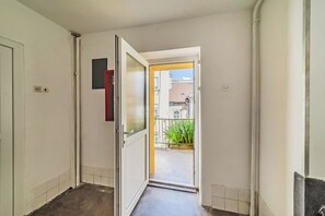 Un pasillo con una puerta que da a un balcón, con vistas a edificios y plantas.