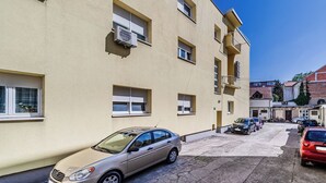 En flervåningsbyggnad med bostäder, utrustad med luftkonditioneringsanläggningar, ett parkeringsområde med flera bilar och en klarblå himmel.