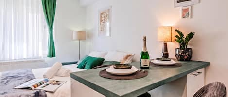 A hotel room with a bed, a small table with a bottle of champagne, a lamp, and a plant.