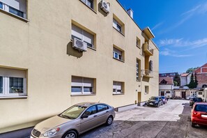 Ein mehrgeschossiges Wohngebäude mit Klimaanlagen, einem Parkplatz und einem roten Auto davor.