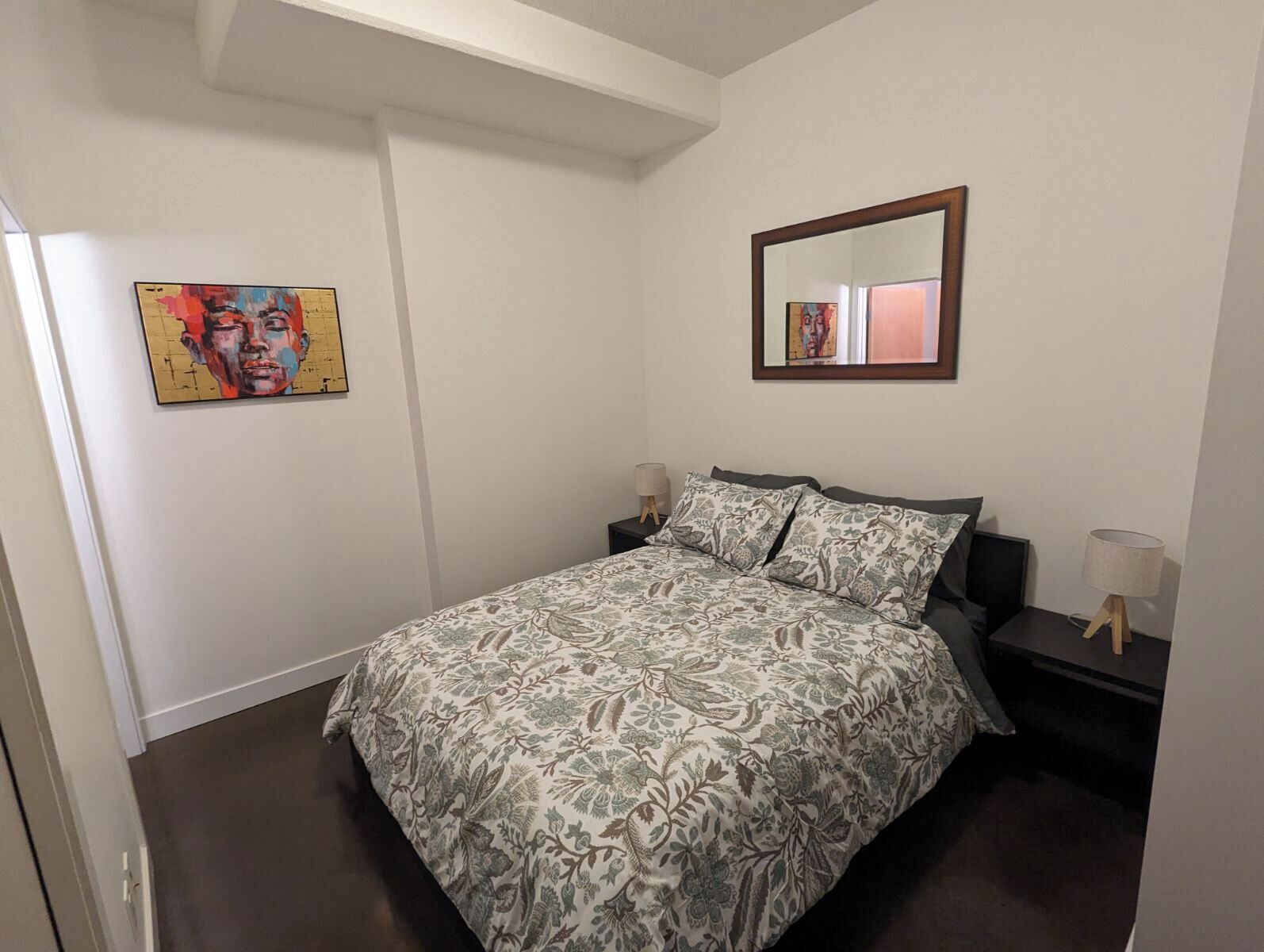 A bedroom with a bed, two bedside tables, a mirror, and a painting on the wall.