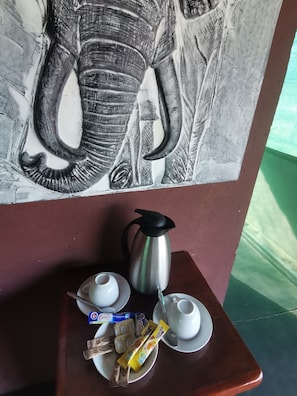 Una mesa con una cafetera, dos tazas, un plato de aperitivos y una decoración en la pared.