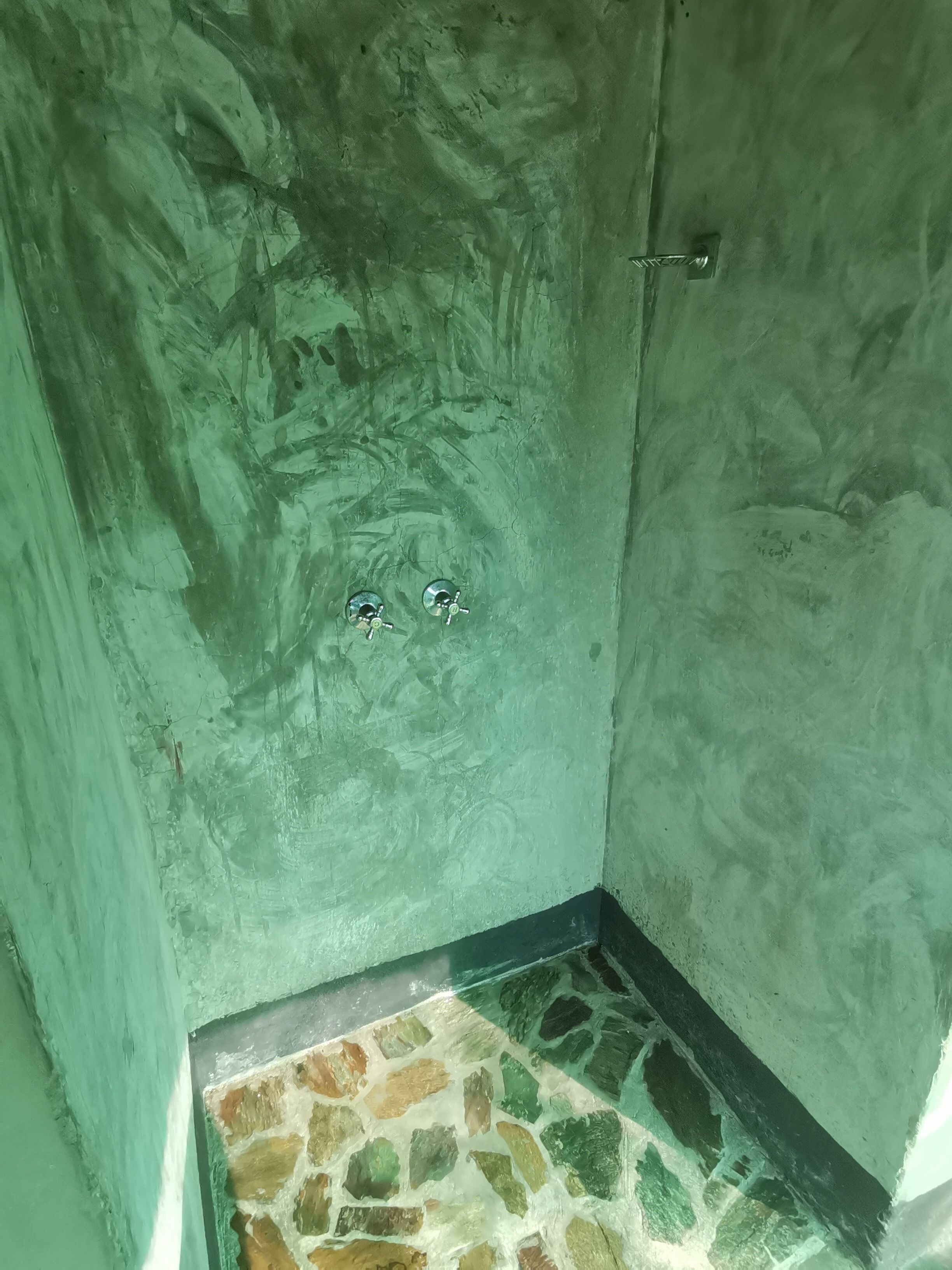 A small, enclosed bathroom with a greenish wall and a stone-tiled floor.