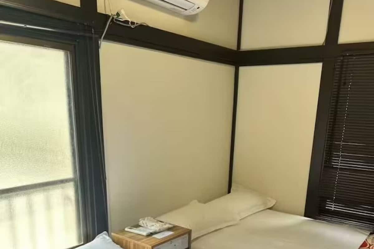 Habitación de hotel con dos camas, una ventana, un equipo de aire acondicionado y una mesita de noche de madera.