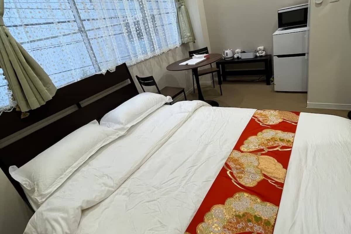 Habitación de hotel con cama, escritorio, silla, unidad de aire acondicionado y ventana con cortinas.