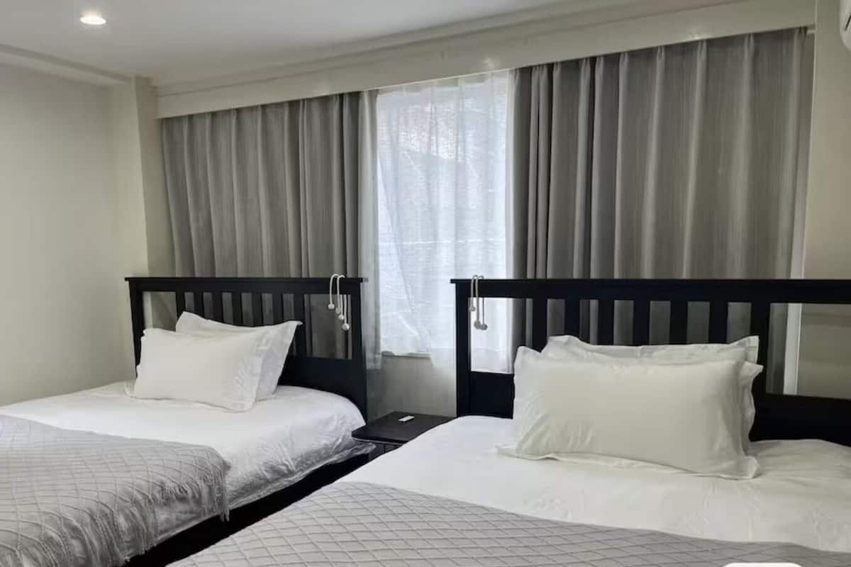 Habitación de hotel con dos camas individuales, una mesita de noche y una ventana con cortinas.