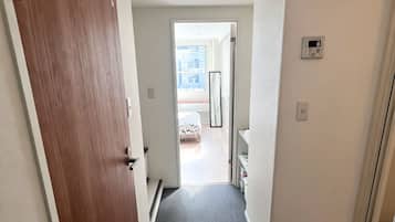 A hallway with a wooden door, carpeted floor, and a white wall with a smoke detector.
