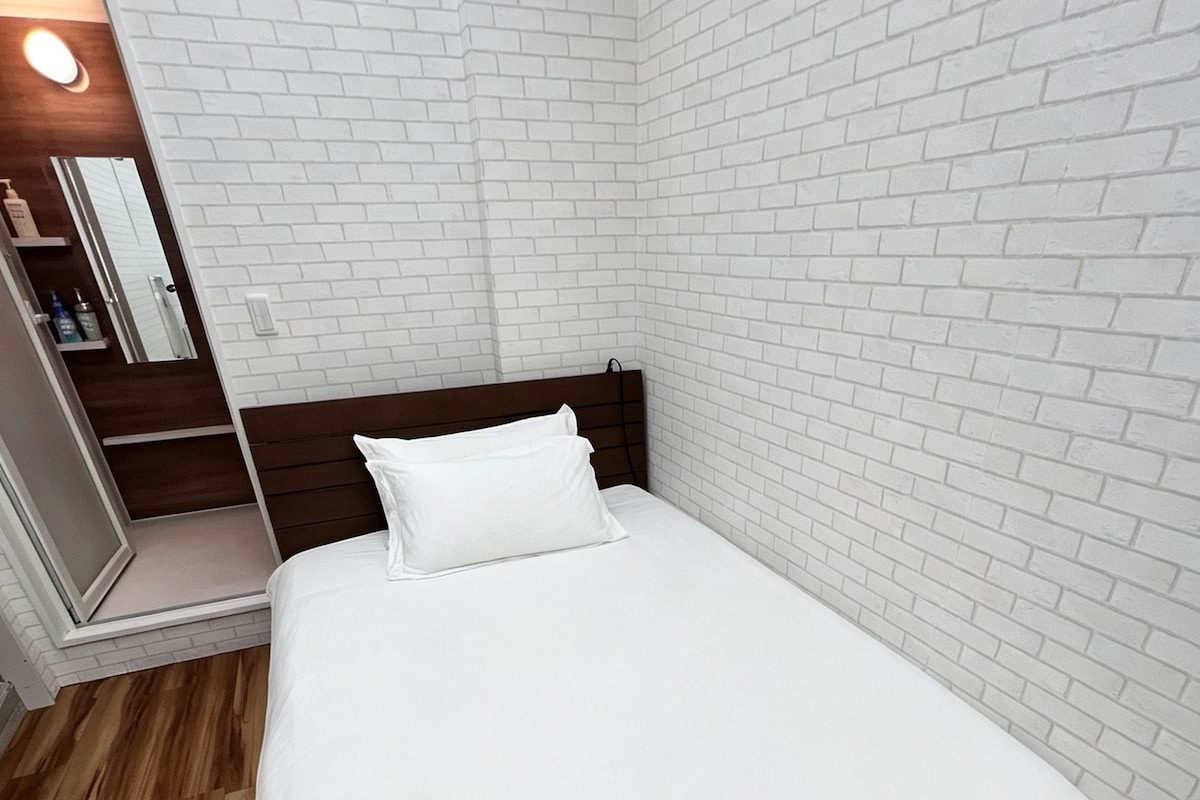 A neatly made bed in a room with white brick walls and wooden flooring.