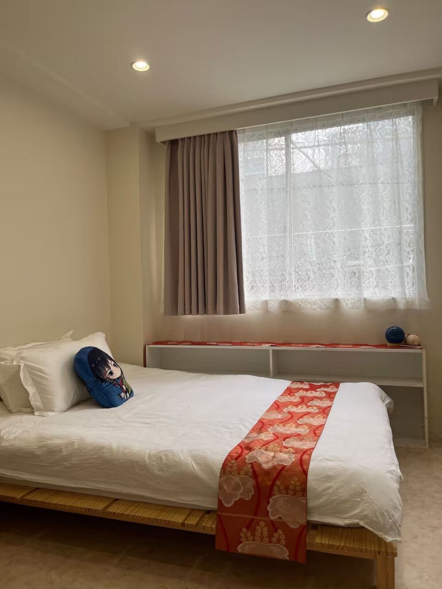 A bedroom with a bed, a window with curtains, a bedside table, and a wall-mounted shelf.