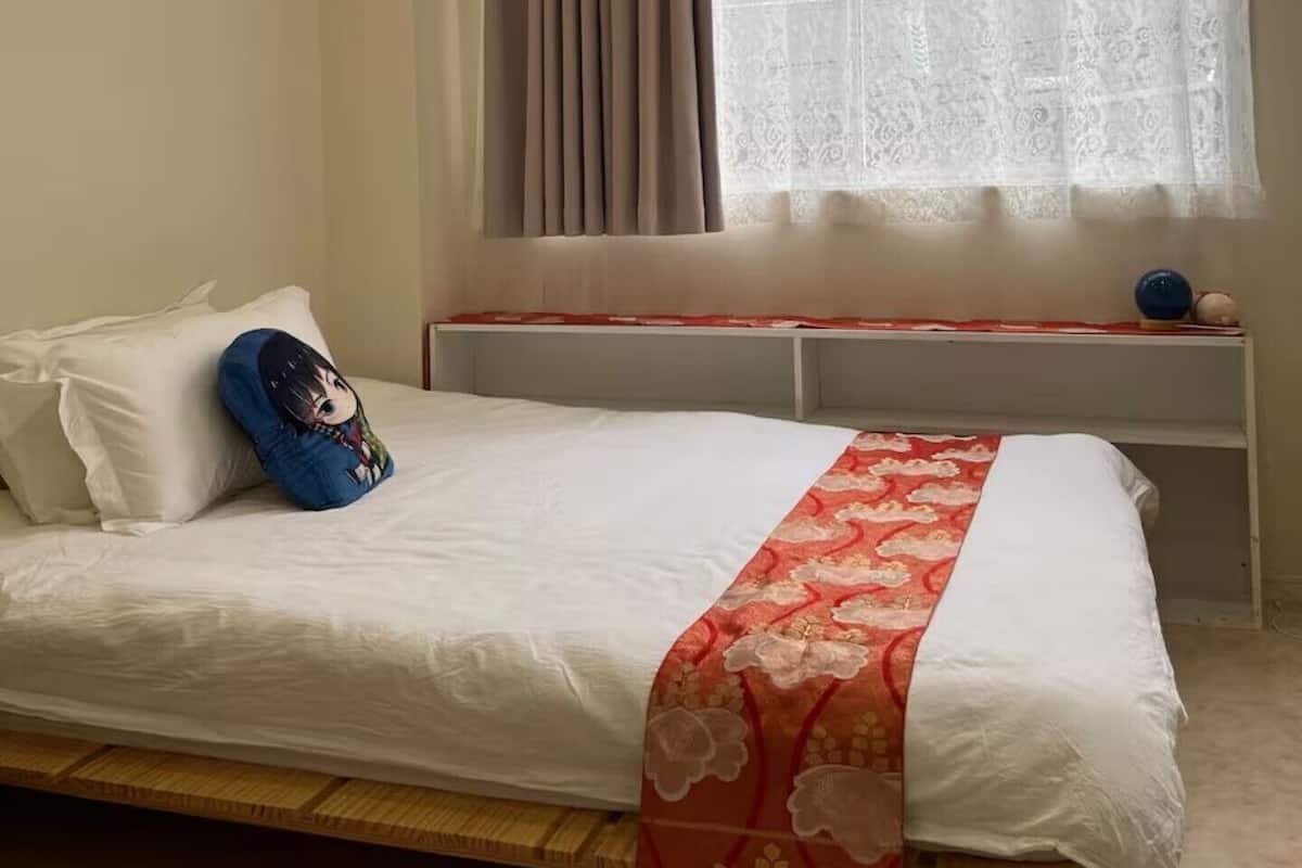 Un dormitorio con cama, ventana con cortinas, mesita de noche y estante en la pared.