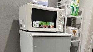 A compact kitchenette with a microwave, a small trash bin, and a shelf with a can of drink.